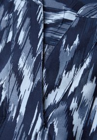 Tessuto blu navy con un motivo testurizzato di pennellate blu chiaro e bianche. Il collo presenta un design a scollatura a V.