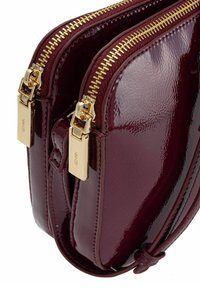 Burgundowa torebka ze skóry lakierowanej z podwójnymi przegródkami, złotymi zamkami błyskawicznymi i wykończeniami hardware. Gładka tekstura z błyszczącym wykończeniem.