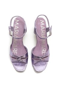 Sandales à talons hauts métalliques violettes avec des lanières croisées, fermeture par boucle, et semelle intérieure texturée comportant le logo. Design à bout carré.