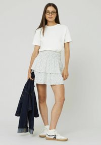 T-shirt blanc, jupe à volants superposés avec un motif floral, veste en jean et baskets blanches avec des accents noirs. Design simple et décontracté.