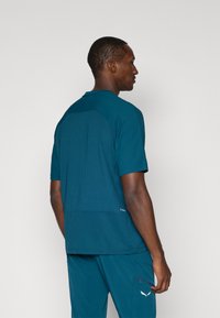 Μακρυμάνικη αθλητική μπλούζα σε απόχρωση τιρκουάζ με ραβδωτή υφή, διαθέτει στρογγυλή λαιμόκοψη και σχέδιο με αντίθεση στο πίσω μέρος.