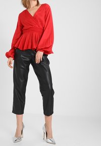 Rød indpakning bluse med lange pufærmer, elastisk talje, kombineret med sorte læder cropped bukser og metallisk sølv høje hæle.