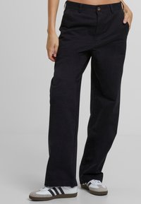 Black wide-leg pants with a smooth fabric, featuring a button closure and front pockets. Paired with white and grey sneakers.