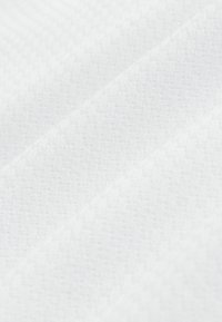 Białe teksturowane tkaniny z subtelnym geometrycznym wzorem, o gładkiej powierzchni i delikatnym połysku, ułożone w złożonych warstwach.