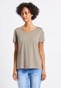 Jasno taupe krótki rękaw t-shirt z szerokim dekoltem i miękką teksturą, w połączeniu z jasnoniebieskimi dżinsami. Prosty, casualowy design.