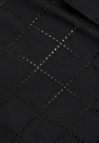 Schwarzer Stoff mit einem Rautenmuster, das entlang der Nähte mit ausgeschnittenen Kreisen versehen ist. Strukturiert mit einer Kombination aus soliden und offenen Elementen.