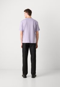 Lys lavendel bomulds T-shirt med korte ærmer og rund hals; parret med mørke lige ben jeans; vist fra ryggen.