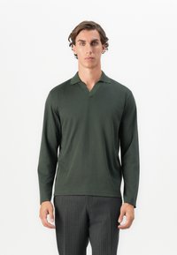 Mørkegrøn langærmet polo-shirt med V-hals og ribbet krave, lavet af glat stof. Bæres med stribede bukser.