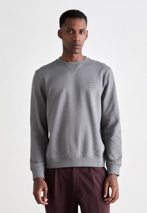 Sweatshirt gris avec un col rond, des poignets et un ourlet côtelés. Présente un petit logo brodé sur la poitrine, fabriqué en tissu doux.
