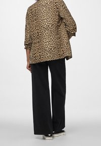 Camisa oversized de leopardo en beige y negro, combinada con pantalones anchos negros y zapatillas negras con suelas blancas.