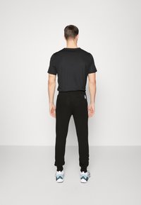 Sort bomulds t-shirt med korte ærmer, parret med sorte joggers. Joggersne har en tætsiddende manchet. Sneakers har blå og hvide accenter.
