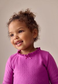 Top morado de manga larga con un escote con volantes y un pequeño lazo rosa como detalle, hecho de un material suave y texturizado. Adecuado para niños.