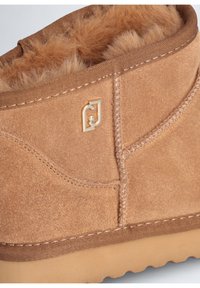 Stivaletti alla caviglia in suede color tostato con morbida fodera in tinta, dettaglio del logo dorato e rifiniture cucite. Presenta una suola testurizzata per una migliore aderenza.