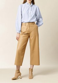Blusa a righe blu e bianche con colletto arricciato e maniche a palloncino, abbinata a pantaloni in pelle beige a gamba larga e stivaletti coordinati.