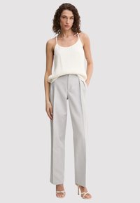 Top bianco senza maniche con spalline sottili abbinato a pantaloni grigi chiari plissettati, dotati di tasche laterali e una vestibilità rilassata.