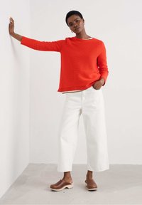 Maglione rosso a coste, pantaloni bianchi a gamba larga e zoccoli marroni. Il maglione ha un collo a giro e maniche lunghe con una vestibilità comoda.
