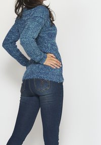 Pull en laine bleu avec un motif texturé, coupe ajustée, manches longues et ourlet à franges, associé à un jean skinny bleu foncé.