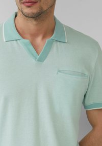 Licht mintgroene polo shirt van gestructureerde stof, met een V-hals, witte afwerking op de kraag en een klein borstzakje.