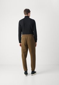 Schwarzes Langarmshirt, kombiniert mit braunen schmal geschnittenen Jogginghosen mit elastischem Bund und zwei hinteren Taschen, getragen mit schwarzen High-Top-Sneakern.