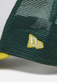 Gorra de malla verde con un logo bordado en blanco y amarillo, y un acento amarillo en contraste a lo largo del borde.