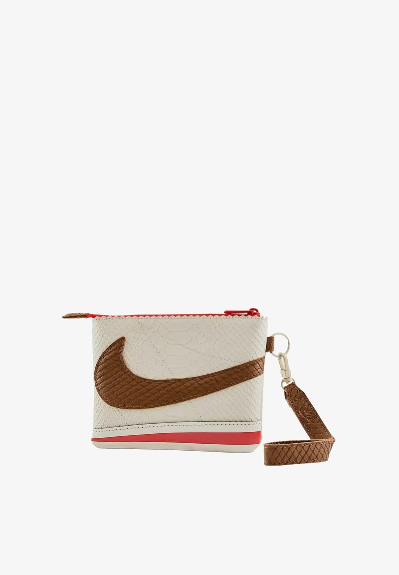 Pochette Nike realizzata in pelle bianca testurizzata con un logo swoosh marrone. Presenta una cerniera rossa e un cinturino da polso marrone staccabile.
