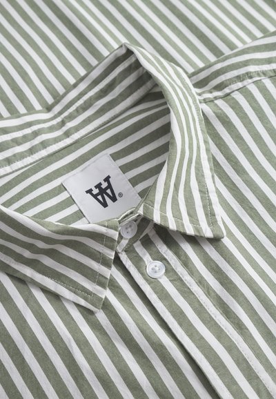 Green and white vertically striped button-up shirt with collar and white buttons, showing a brand label with black lettering inside the collar.