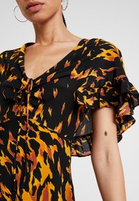 Svart klänning med abstrakt tryck i orange och gult, v-ringning, knytdetalj fram och volangärmar. Slät tygtextur.