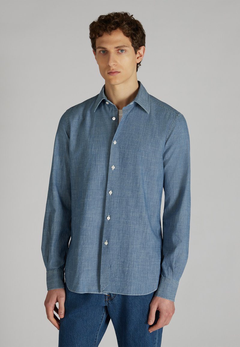 Camicia leggera azzurro chiaro con bottoni, realizzata in tessuto morbido. Presenta un colletto a punta, maniche lunghe e un orlo leggermente curvo. Bottoni bianchi visibili.