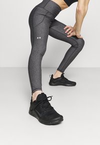 Czarne legginsy sportowe z teksturowanego materiału i wysokim stanem, z małym białym logo. Czarne buty treningowe z siateczkową cholewką.