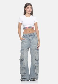 T-shirt bianca a maniche corte con una fascia logata nera e rossa. Jeans cargo blu chiaro con più tasche, vestibilità ampia, texture di denim sbiadito.