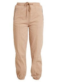 Beżowe spodnie dresowe wykonane z miękkiej bawełny. Posiadają elastyczny pas z sznurkiem, boczne kieszenie zapinane na zamek oraz ściągacze na kostkach.
