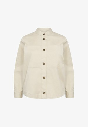 Beidzēs krēms krāsā ar paceltu apkakli, divām priekšējām kabatām un brūnajām pogām. Izgatavots no mīksta, viegla auduma.