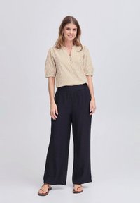 Beige stribet bluse med korte puffærmer, knaplukning, parret med løse sorte brede bukser. Enkle sandaler fuldender looket.