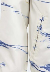 Beige tyg med blå och gula abstrakta vågiga mönster, med en synlig söm och en sidoficka på högra sidan.