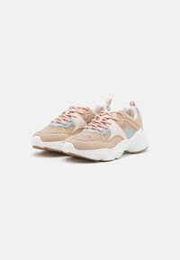 Keve sneakers dengan bagian atas jaring beige, aksen biru pucat, dan tali sepatu merah muda. Memiliki sol putih tebal dan permukaan yang tekstur.