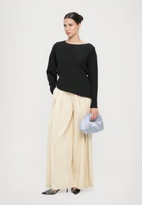 Black long-sleeve top, beige pleated trousers, and a light blue satin clutch. Black pointed-toe heels, minimalist design, and soft textures.