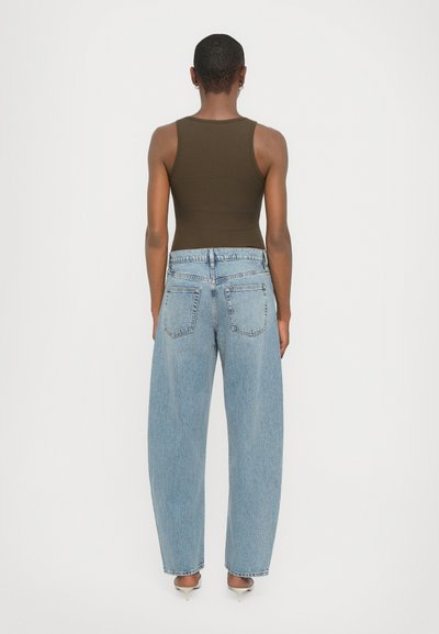 Top aderente marrone e jeans azzurri larghi, con vita alta e taglio dritto, dotati di tasche posteriori standard.