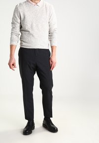 Ljusgrå prickig tröja, mörka skräddarsydda byxor och svarta skor. Slimmad passform, rund halsringning och manschettärmar på tröjan.