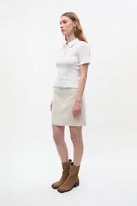 Cămașă polo albă, fustă mini bej și cizme de gleznă din suede maro cu toc gros. Design simplu și textură netedă. Vedere laterală.