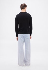 Μαύρο πουλόβερ από μαλακό υλικό, με στρογγυλή λαιμόκοψη και μακριά μανίκια, συνδυασμένο με ανοιχτό μπλε, άνετα τζιν με πίσω τσέπες.