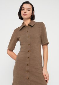 Καφέ πλεκτό φόρεμα με κοντά μανίκια, κουμπιά εμπρός, φαρδύ γιακά και υφασμάτινη υφή. Διαθέτει καφέ κουμπιά κατά μήκος του κέντρου.