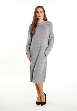Abito maglione grigio a maglia con texture a coste, maniche lunghe e tasche laterali, che arriva a metà polpaccio, abbinato a tacchi alti neri.