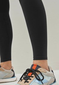 Svarta leggings i stretchmaterial, kombinerade med flerfärgade sneakers med en blandning av beige, blå och orange detaljer.