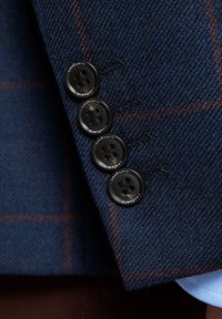 Granatowa marynarka z teksturowanej wełny w kratę, z czterema czarnymi guzikami przy mankietach oraz kontrastowym podszewkiem.