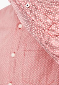 Camisa de manga corta a rayas rojas y blancas con cierre de botón, que presenta un bolsillo en el pecho y un sutil diseño geométrico.