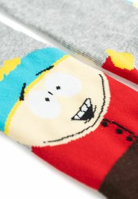 Calze con un design di personaggio su base grigia, un cappello blu, capelli gialli e una maglietta rossa. Materiale a maglia testurizzato con colori brillanti e vivaci.