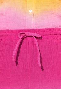 Roze, textieloutfit met textuur, met een verloop van oranje naar roze aan de bovenkant, voorzien van een knoopsluiting en een elastische tailleband met trekkoord.