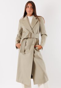 Cappotto beige doppiopetto con vita a cintura, grandi rever e due tasche frontali. Tessuto liscio con vestibilità su misura.