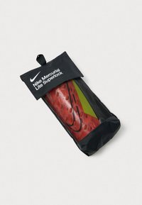 Nike Mercurial Lite Superlock i en sort pouch. Har en rød krop med hexagonal mønster og grønne accenter, lynlåslukning og ophængsslynge.