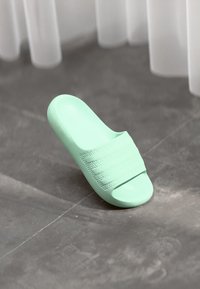 Mint green slide sandal made of textured plastic, featuring three horizontal stripes across the upper. Rounded toe and open back design.